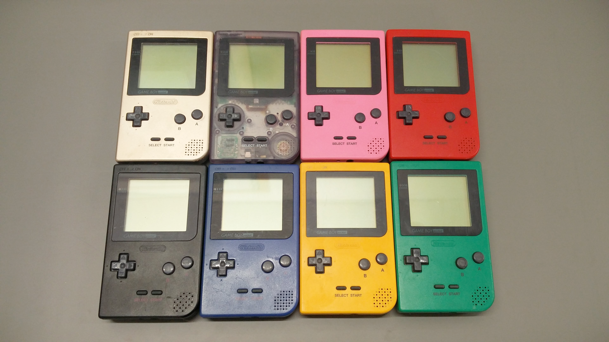 8 Game Boy Pockets in silver, transparent purple, pink, red, black, blue, yellow, and green